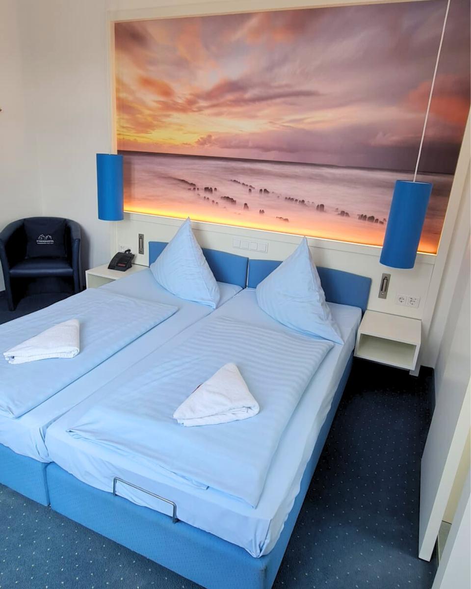 Zimmer mit Doppelbett, Wandbild und blauen Nachttischen.