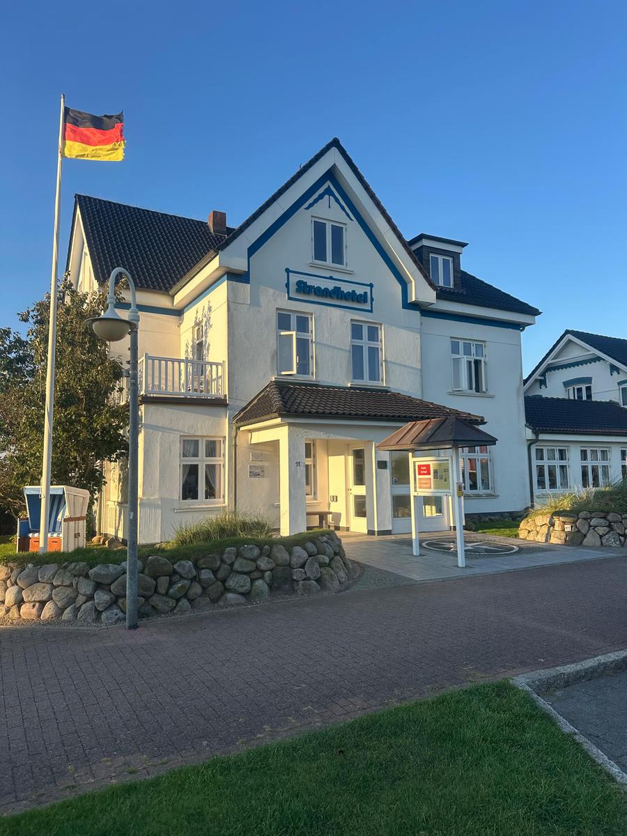Strengelhafen Hotel mit Eingang, Flagge und gepflastertem Vorplatz.