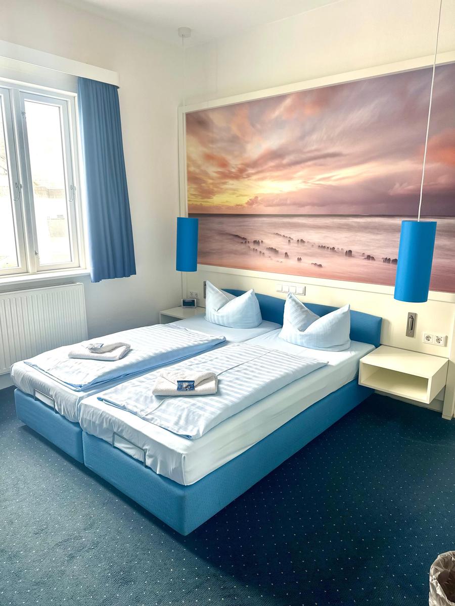 Zimmer mit Doppelbett, Wandbild und blauen Lampen.
