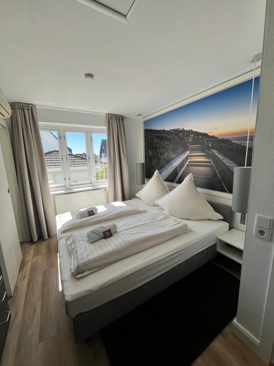 Schlafzimmer mit Doppelbett, Fenster und Wandbild. Holzboden und Nachttische.