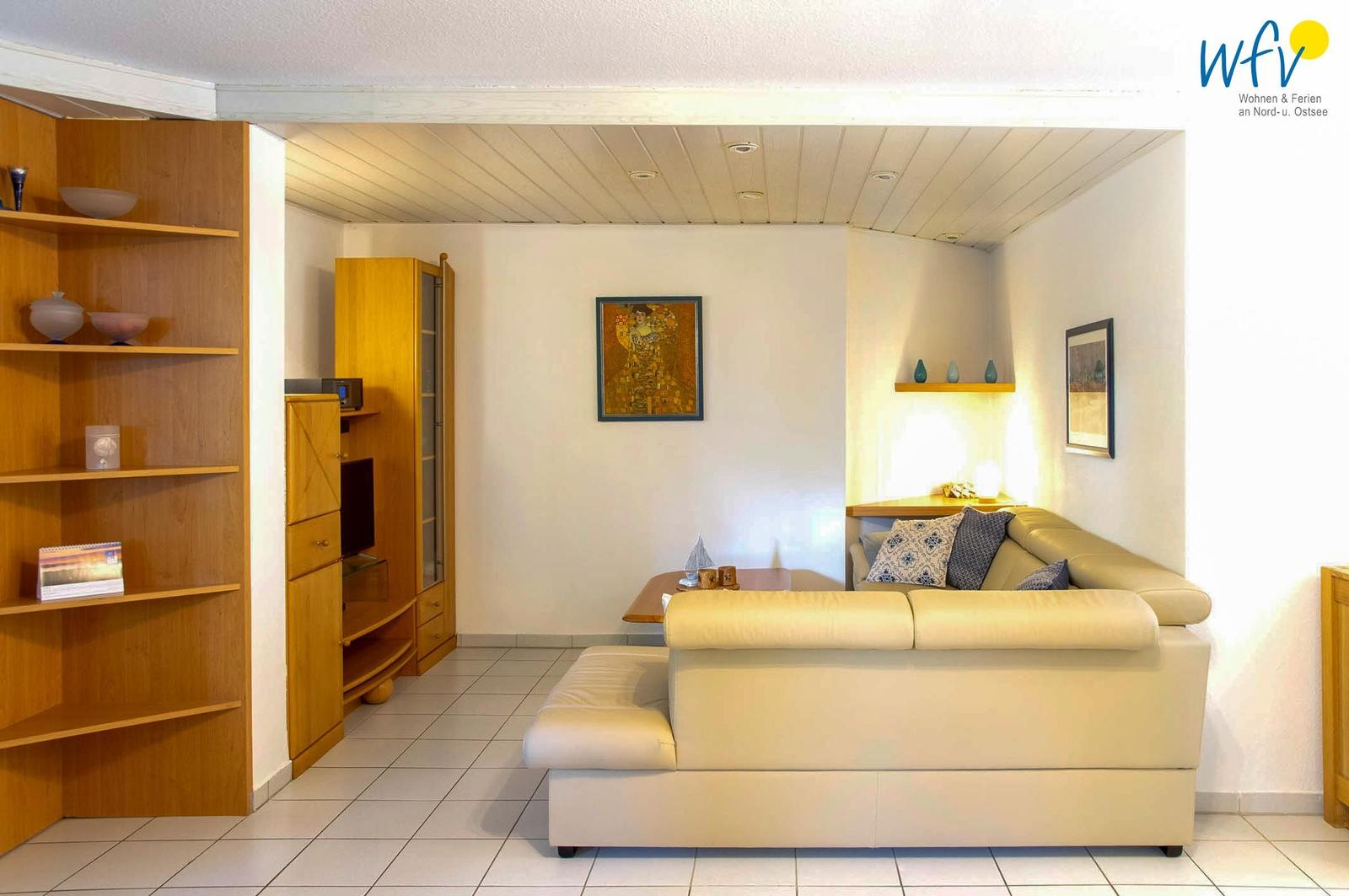 Wohnzimmer mit Sofa, Bücherregal und Wandbild. Holzmöbel und Fliesenboden.