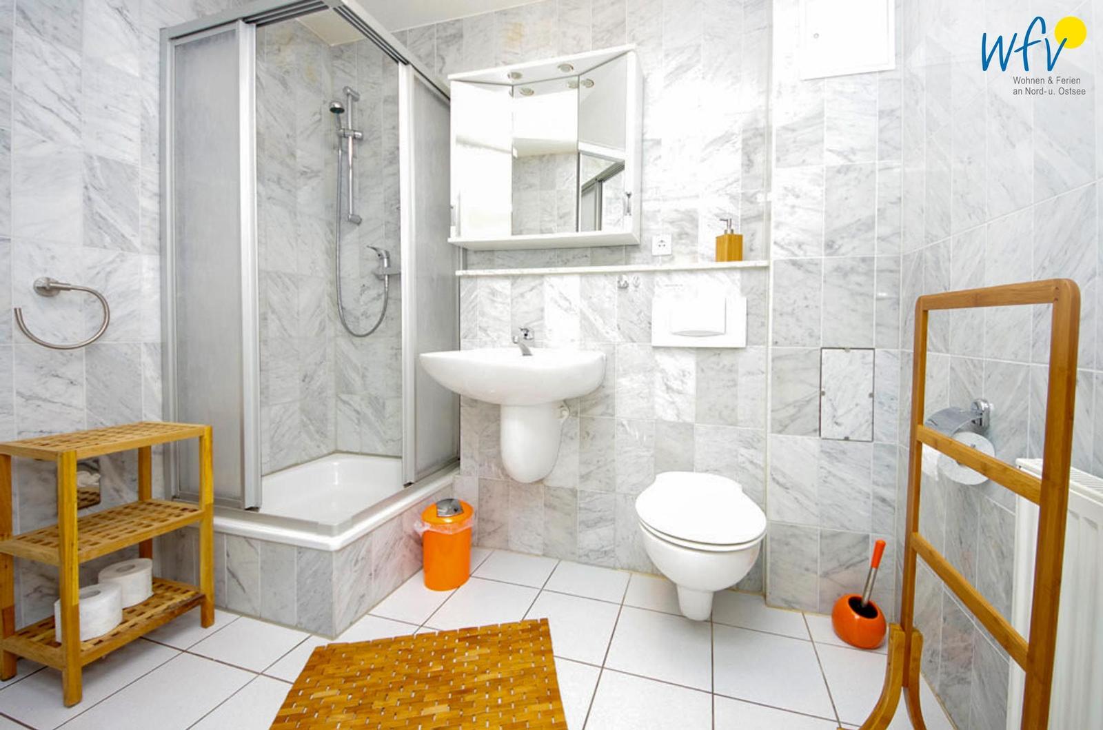 Badezimmer mit Dusche, Waschbecken und WC. Holzregal und Badematte.