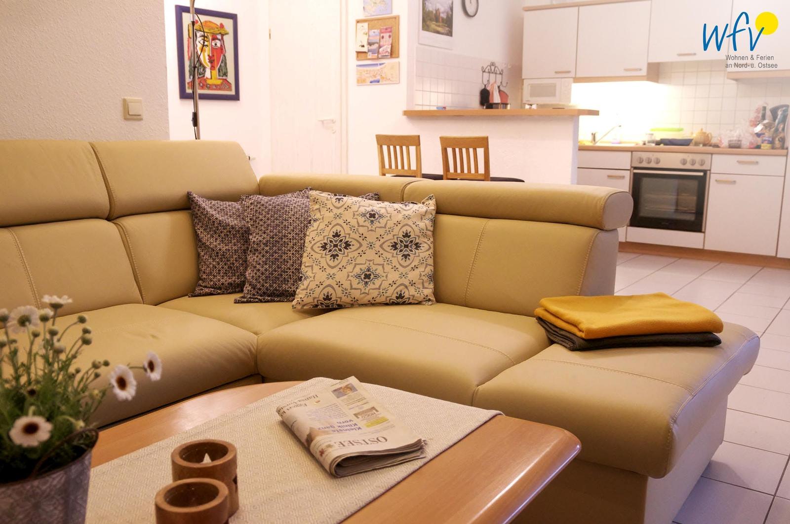 Ein Wohnzimmer mit einem hellen Sofa, Kissen und einem Holztisch mit Zeitung.