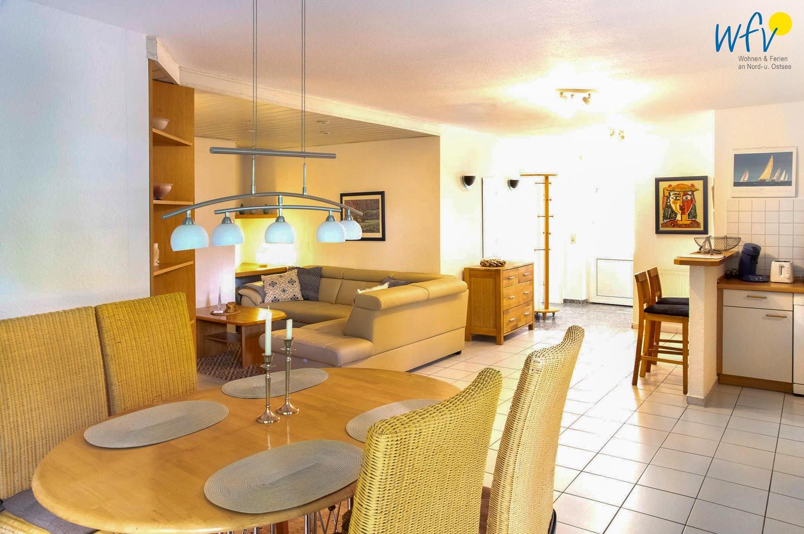 Wohnzimmer und Essbereich mit Holztisch, Stühlen und Sofa. Küche mit Arbeitsplatte und Stühlen.