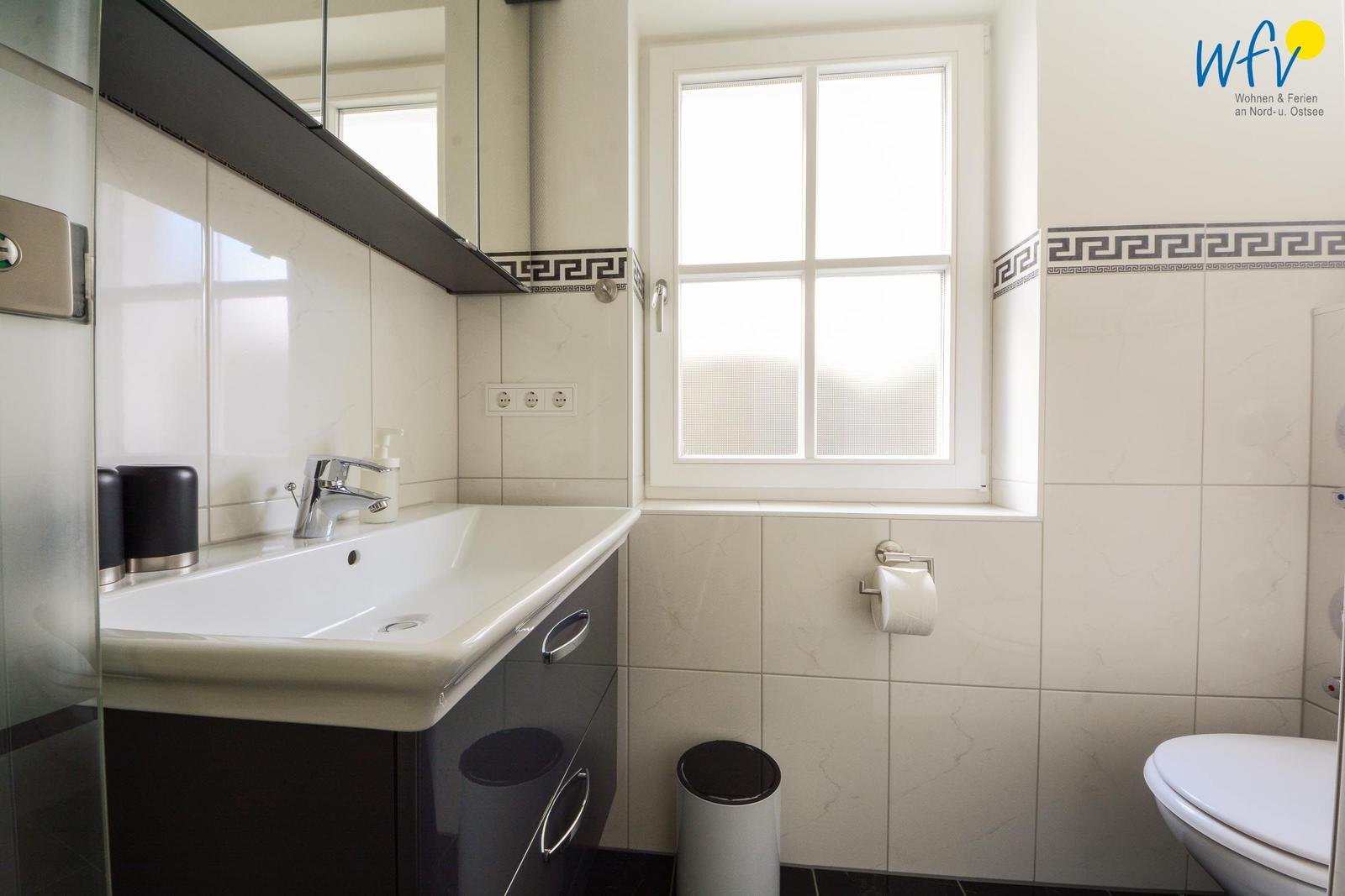 Badezimmer mit Waschbecken, Spiegel, Toilette und Fenster