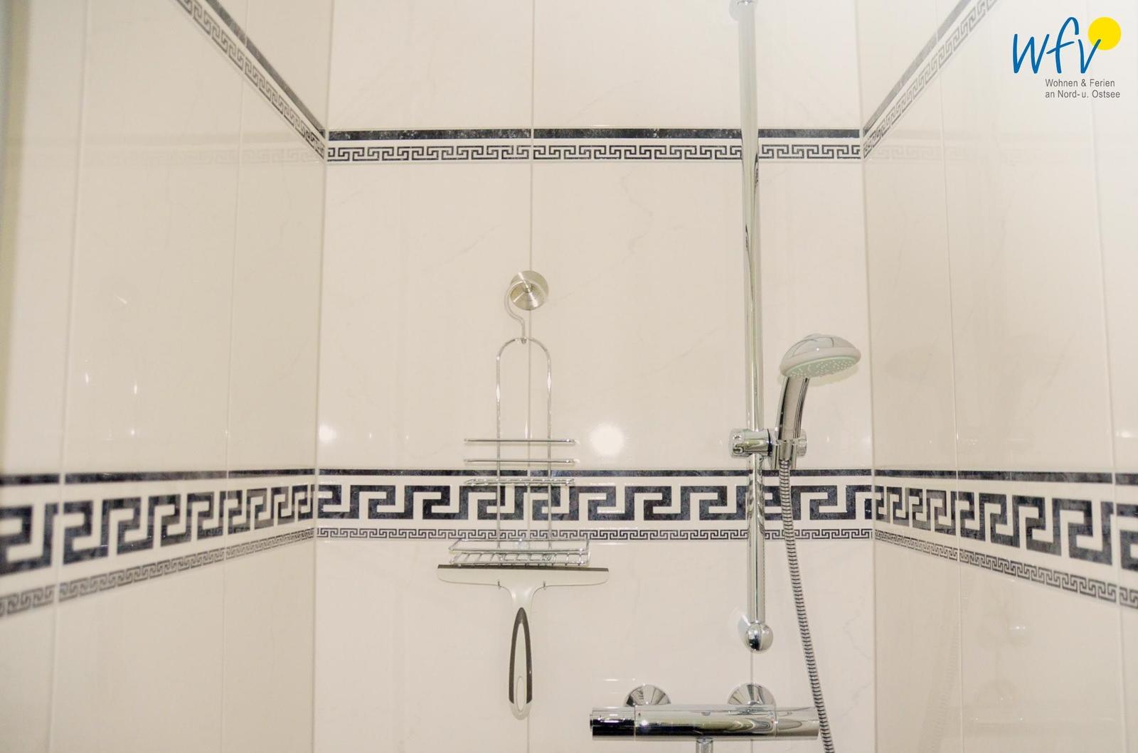 Dusche mit chromfarbenem Duschset und dekorativen Fliesenstreifen.