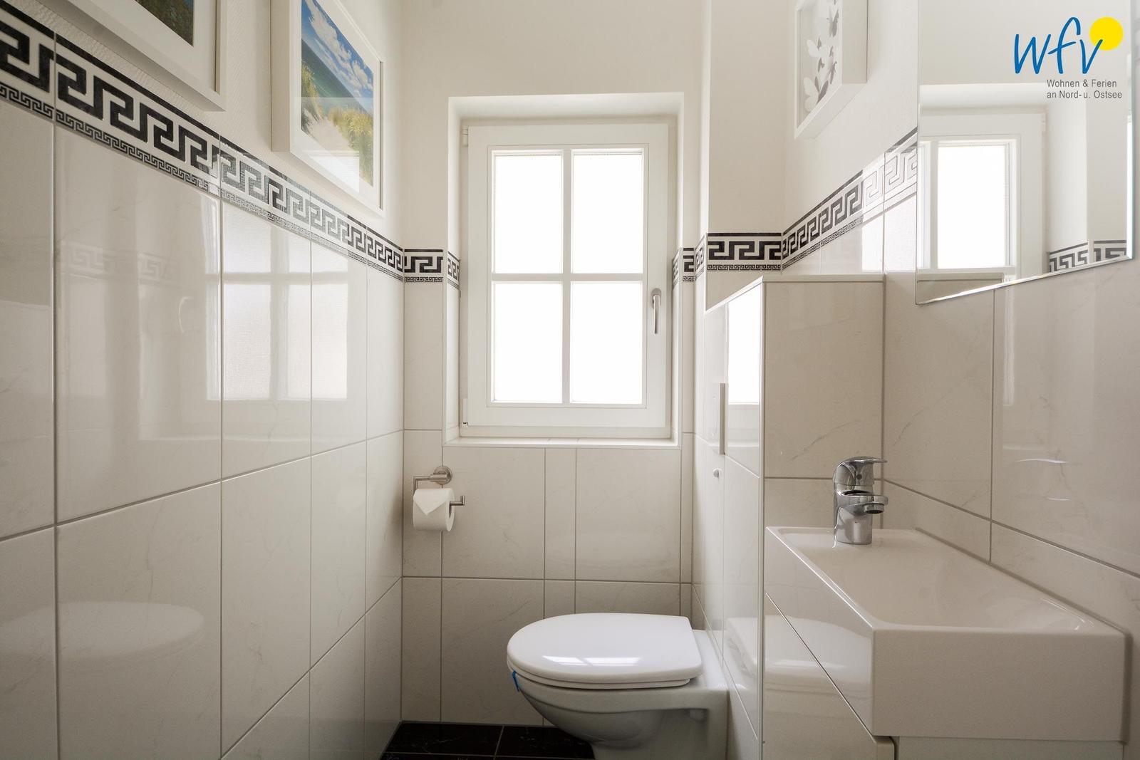 Badezimmer mit Toilette, Waschbecken und Fenster. Wandfliesen mit griechischem Muster.