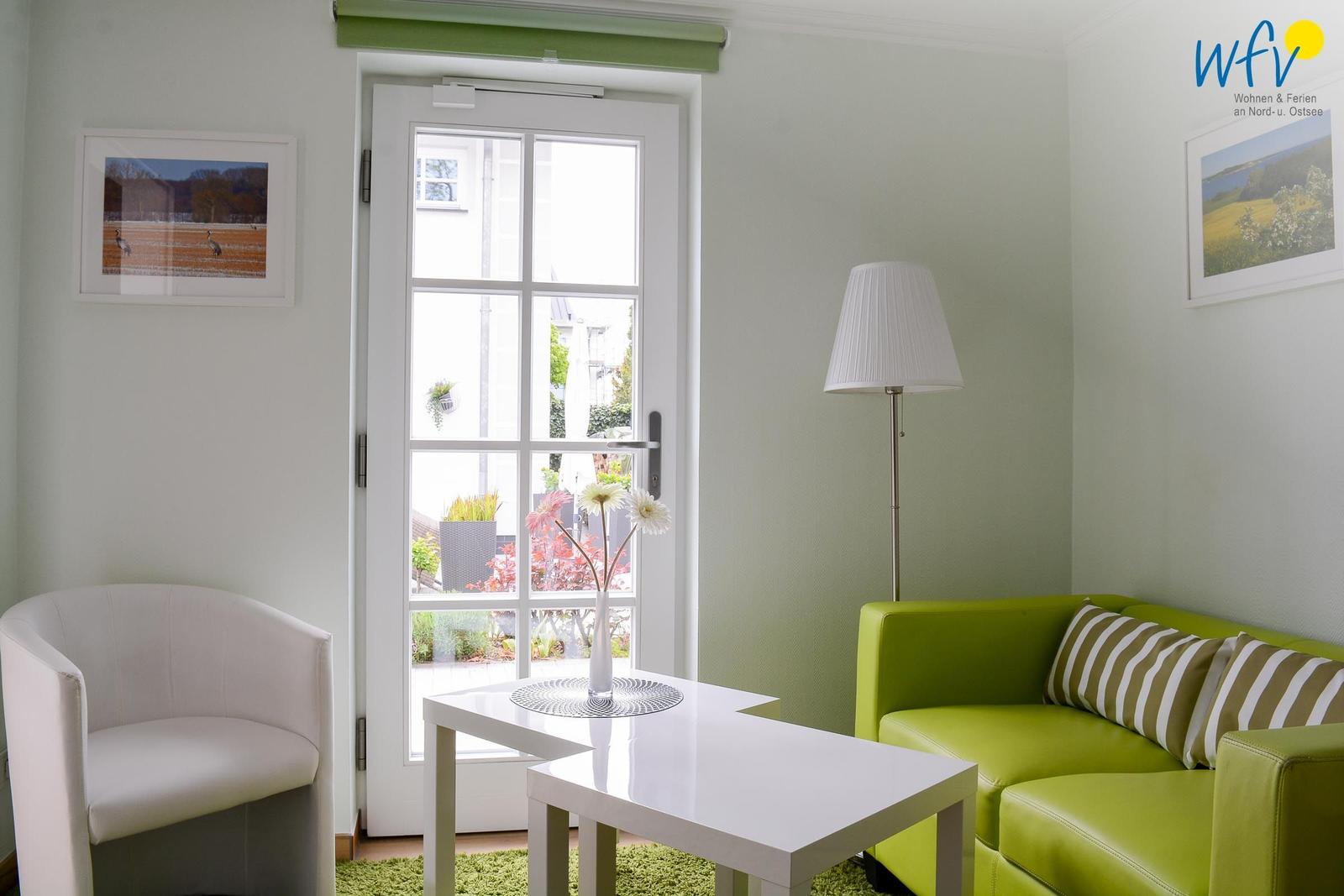 Ein Wohnzimmer mit grünem Sofa, weißer Couch und Fenster zur Außenterrasse.