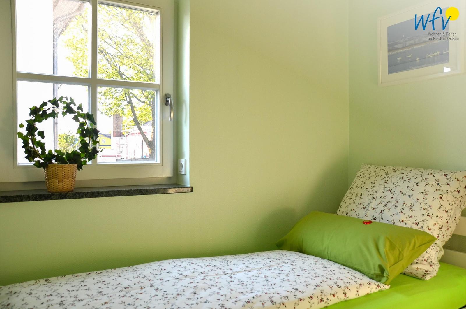 Ein Schlafzimmer mit grünen Wänden, einem Bett mit Kissen und einem Fenster mit Pflanze.