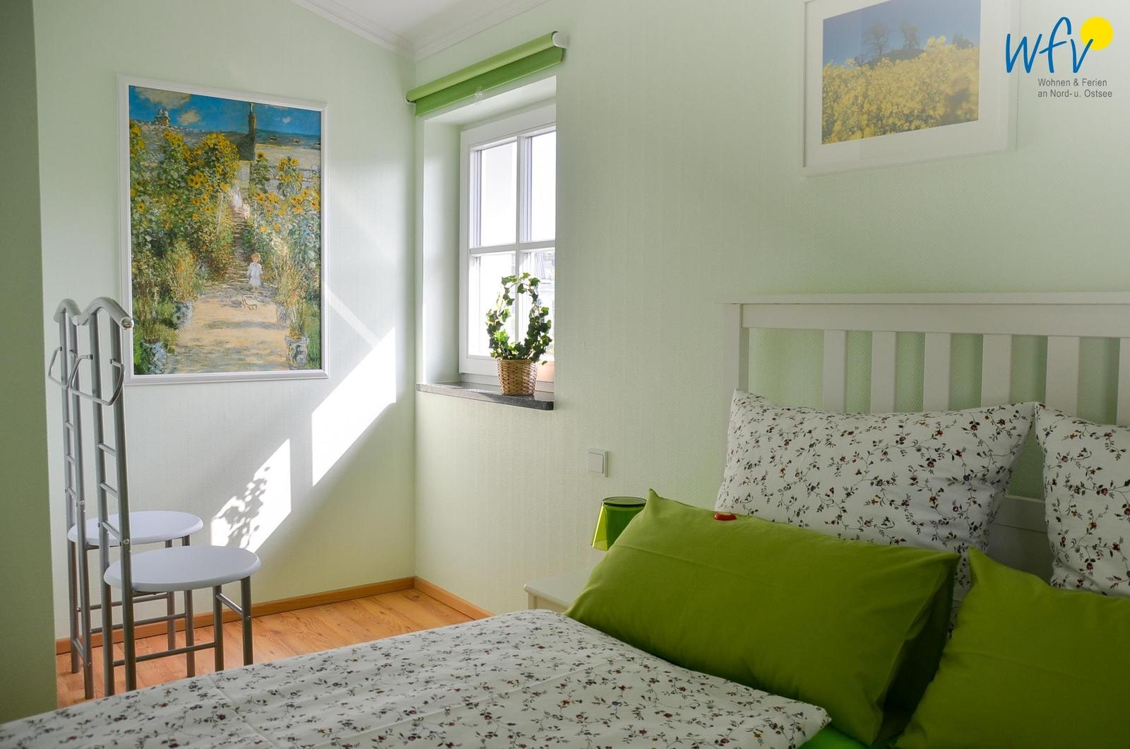 Schlafzimmer mit Bett, Fenster, Bildern und Kleiderständer.