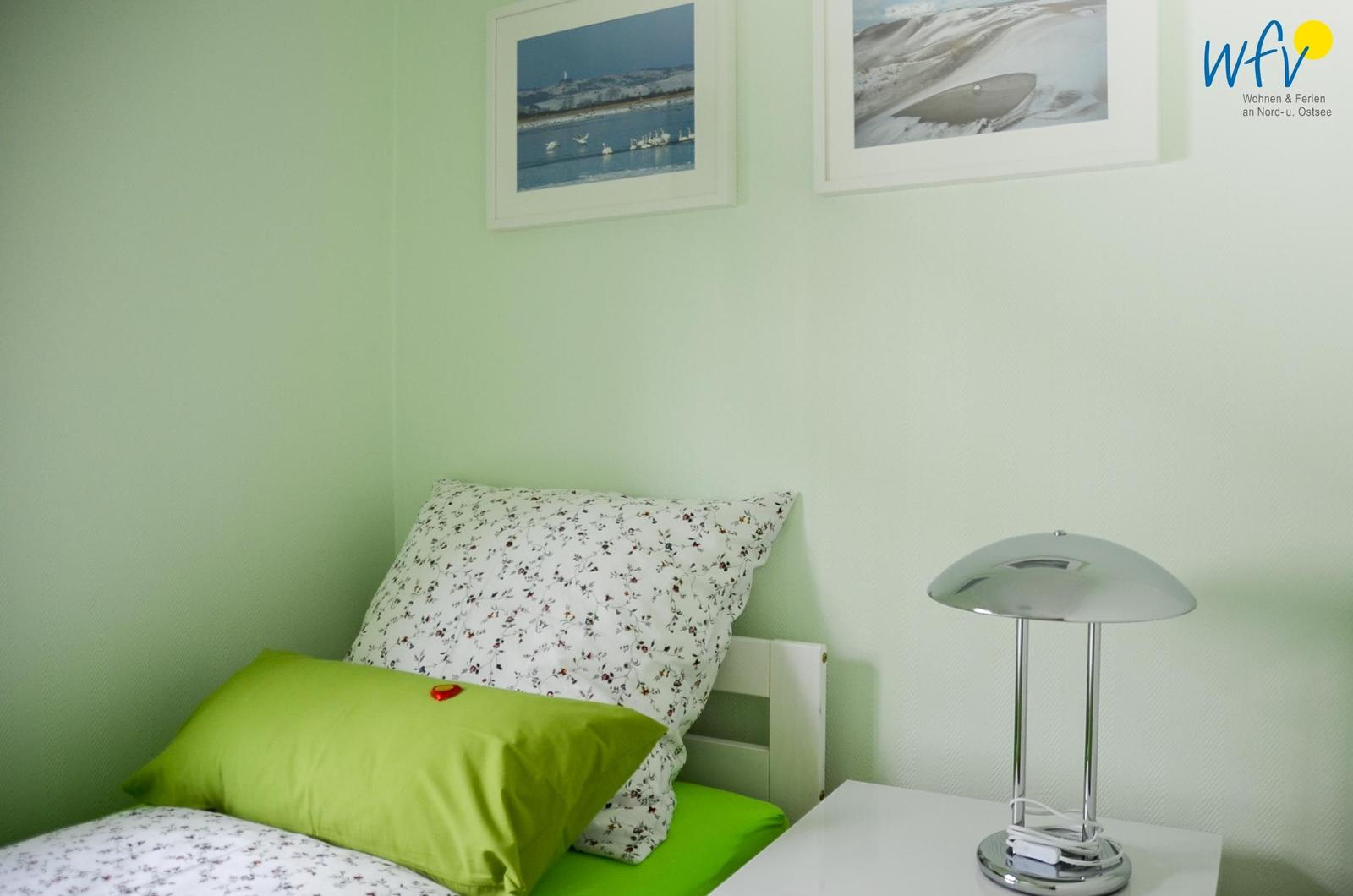 Schlafzimmer mit grüner Wand, Bett mit Kissen und Nachttisch mit Lampe.