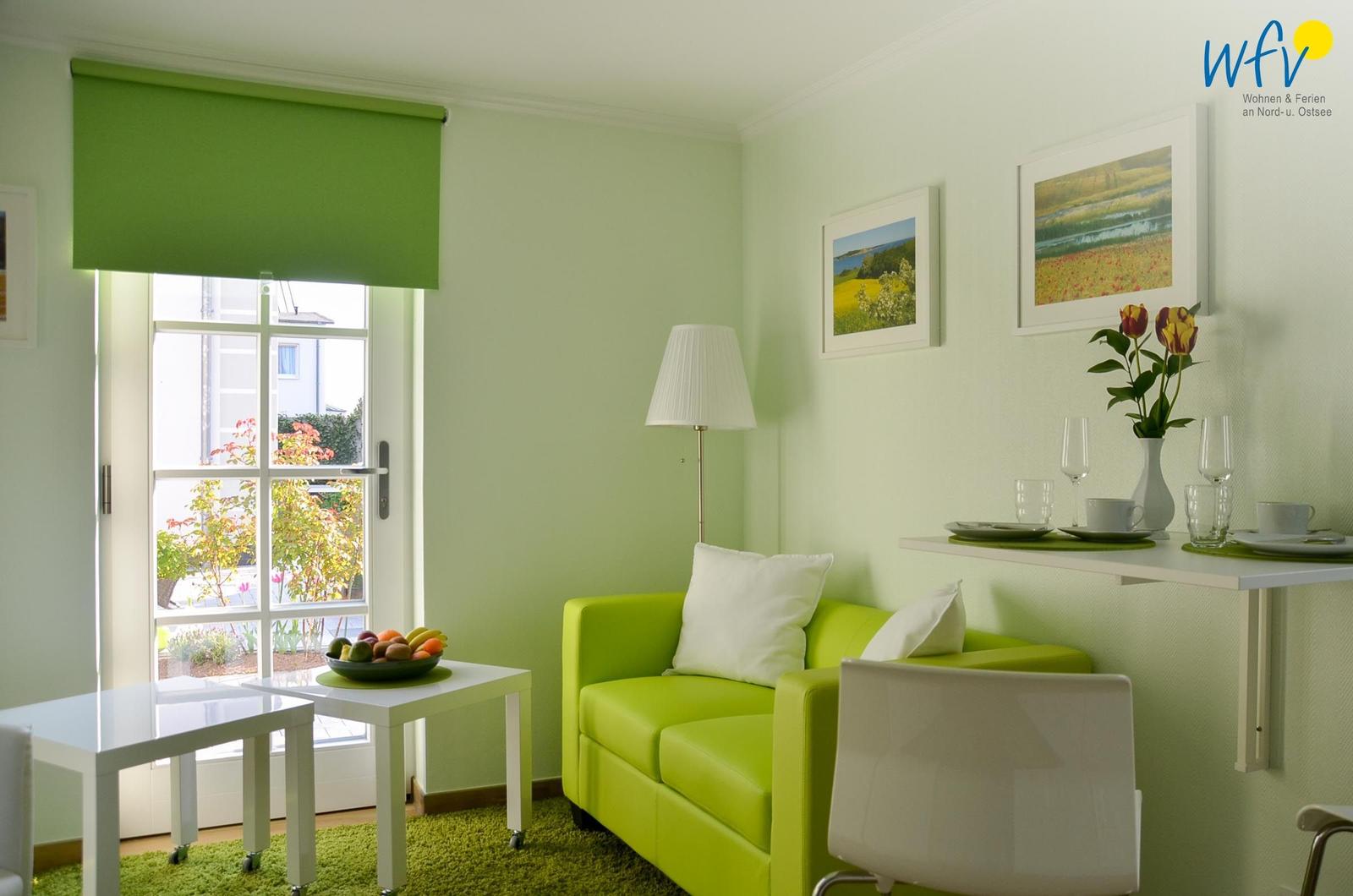 Ein Wohnraum mit grünem Sofa, weißen Möbeln und Fensterblick auf Außenbereich.