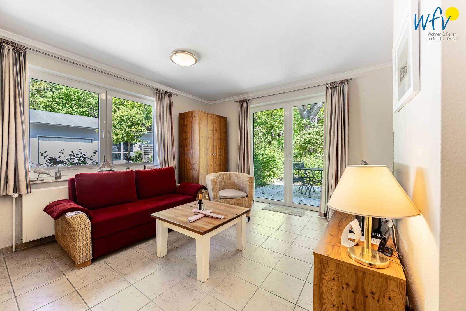 Ein Wohnzimmer mit rotem Sofa, Holztisch und Glastüren zur Terrasse.