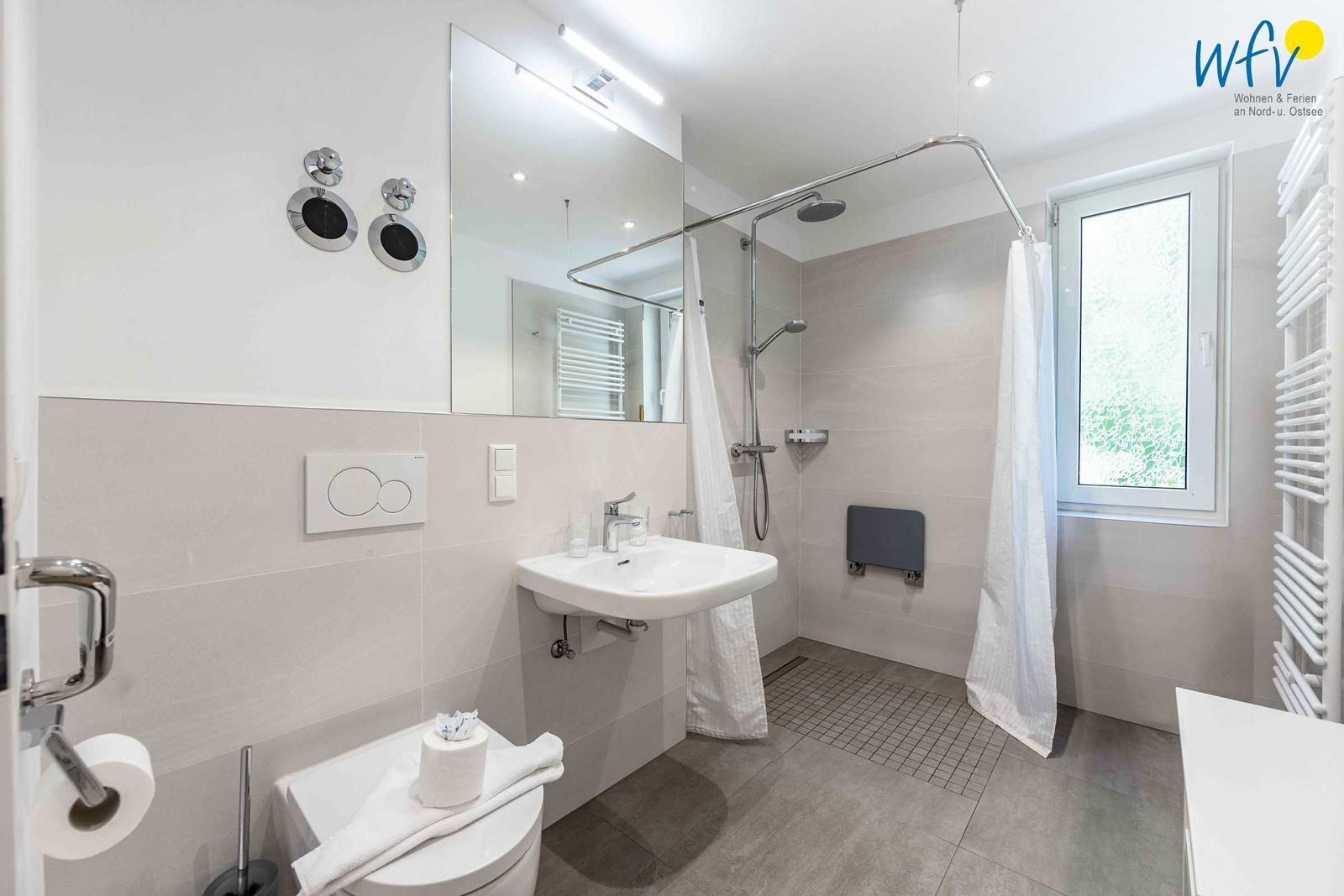 Badezimmer mit Dusche, Waschbecken und Toilette. Fenster und Heizung sind vorhanden.