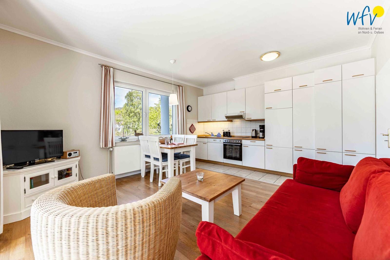 Wohnzimmer mit rotem Sofa, Esstisch und Küche im Hintergrund.