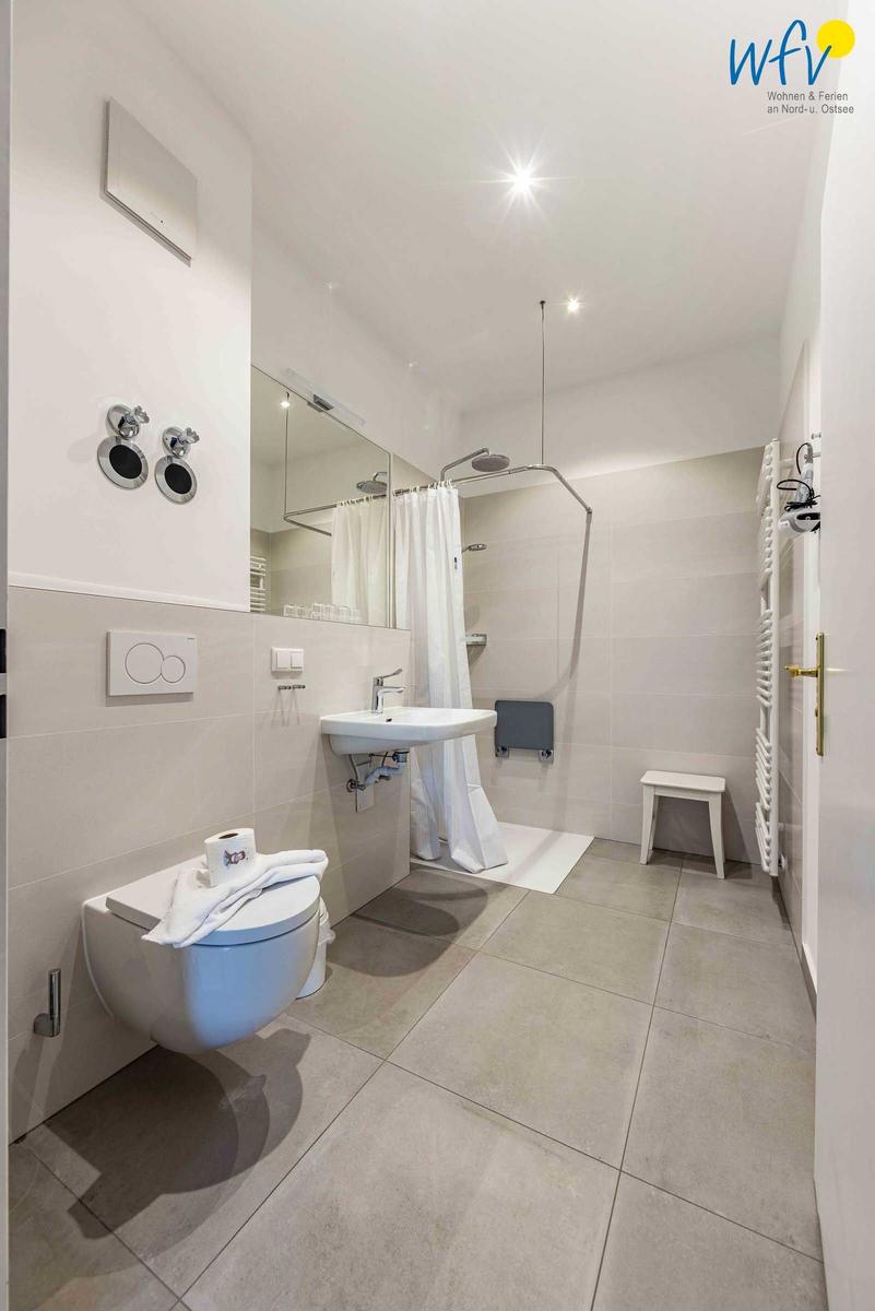 Badezimmer mit Dusche, Waschbecken und Toilette. Weiße Fliesen und modernes Design.