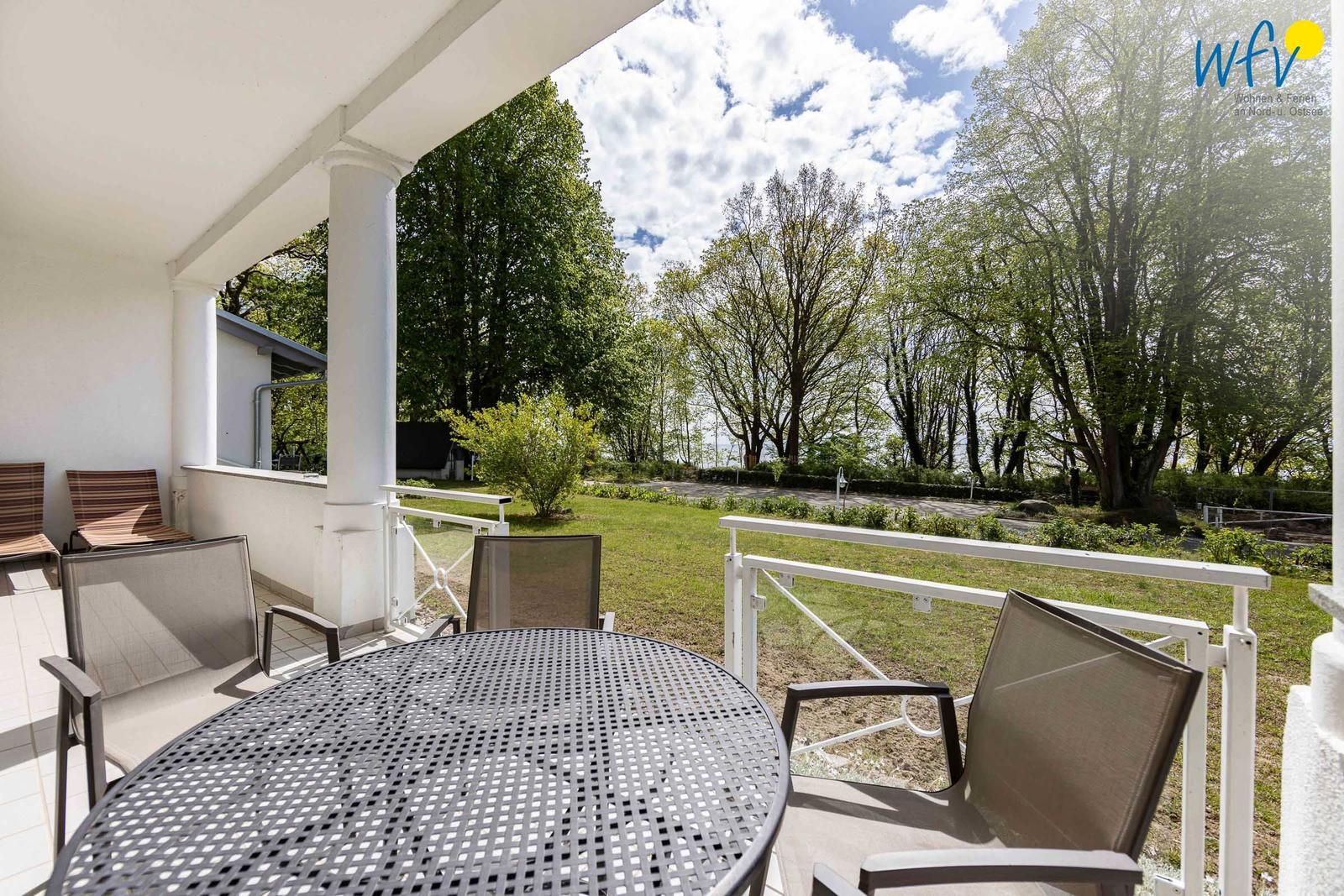 Terrasse mit Tisch und Stühlen, Blick auf Grünflächen und Bäume.