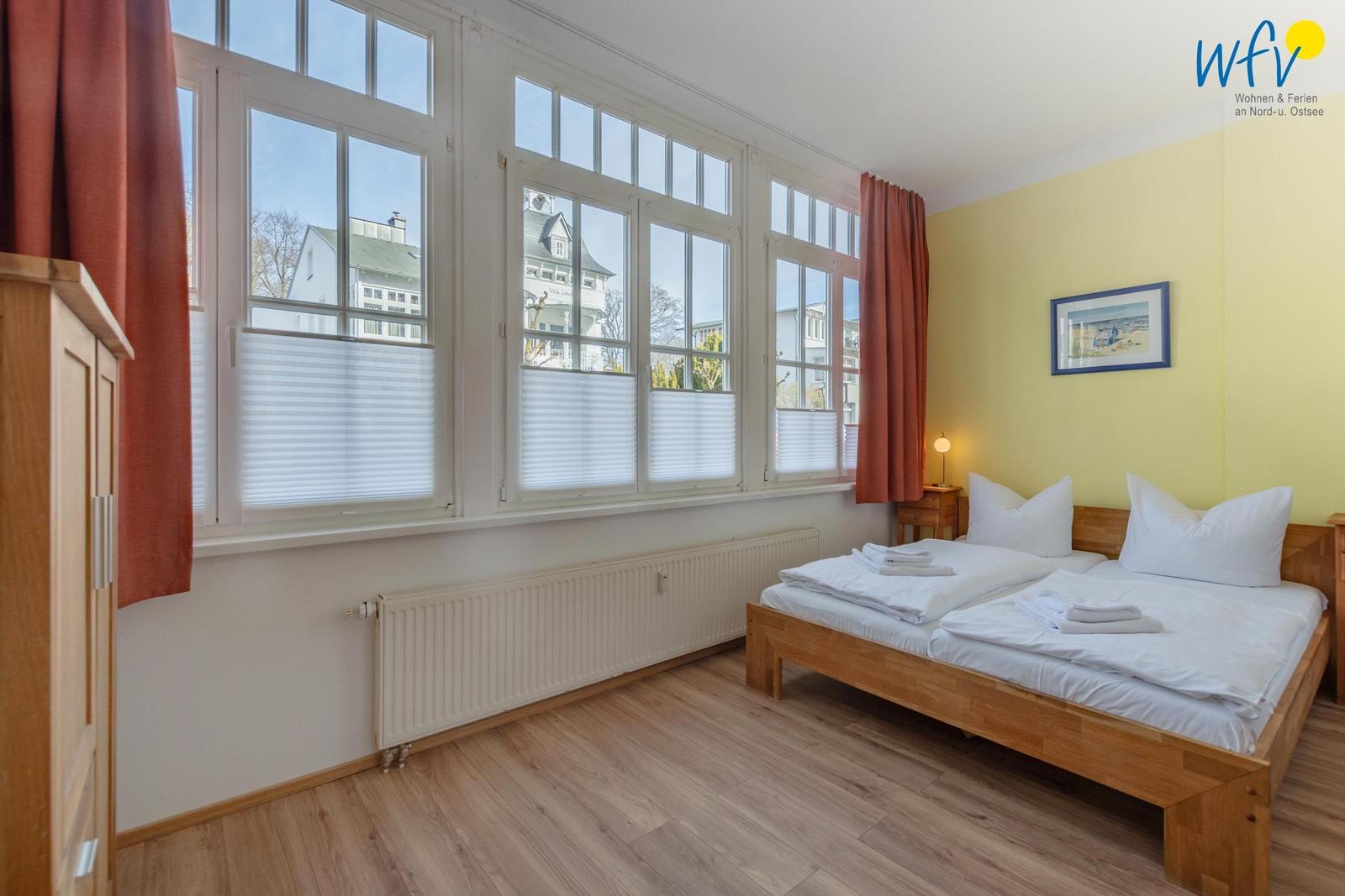 Ein Schlafzimmer mit Holzbett, großen Fenstern und gelber Wand.