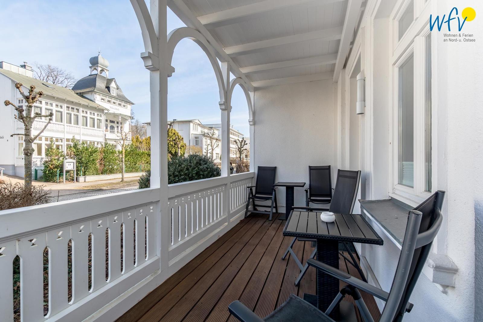 Terrasse mit Tisch und Stühlen, Blick auf Gebäude und Bäume.