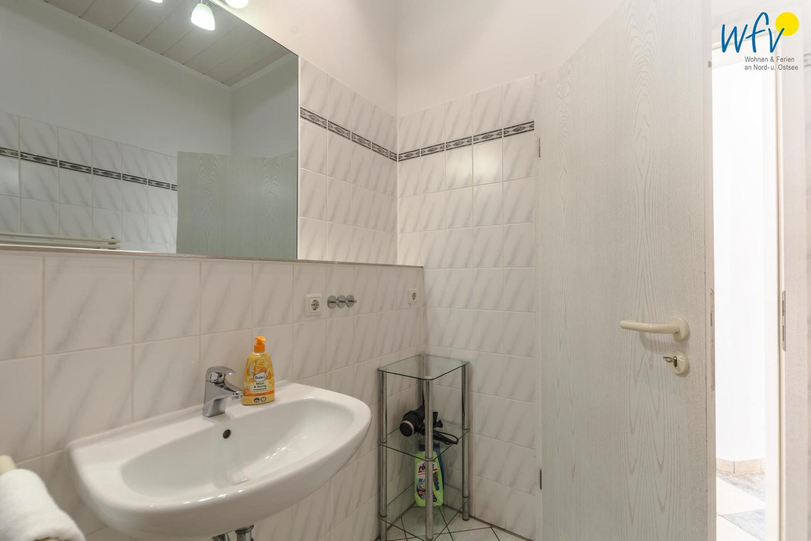 Badezimmer mit Waschbecken, Spiegel und Glasregal.