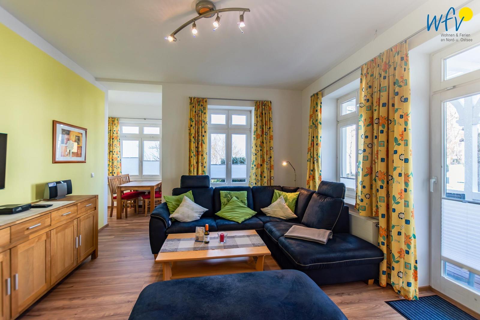 Wohnzimmer mit Sofa, Couchtisch und Fenstern mit gelben Vorhängen.