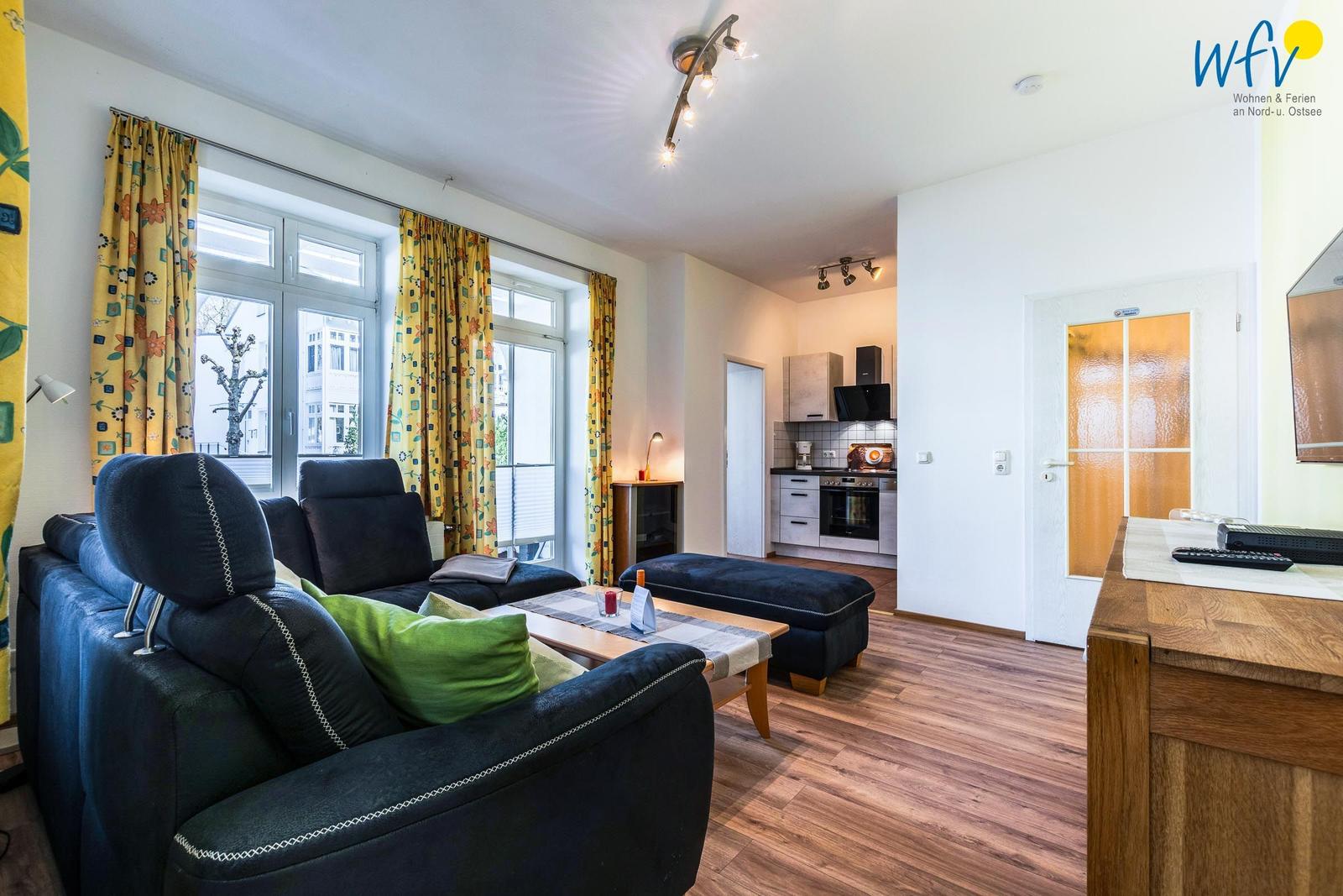 Wohnzimmer mit Sofa, Couchtisch und Küche im Hintergrund.