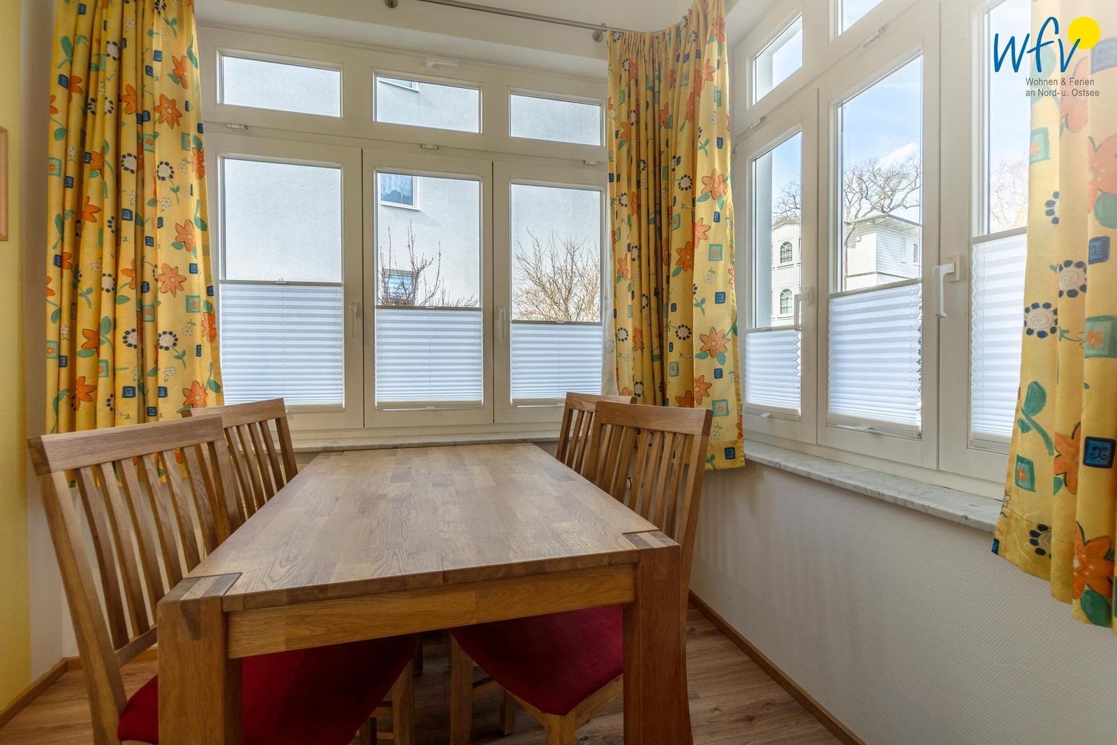 Esszimmer mit Holztisch, Stühlen und großen Fenstern mit gelben Vorhängen.