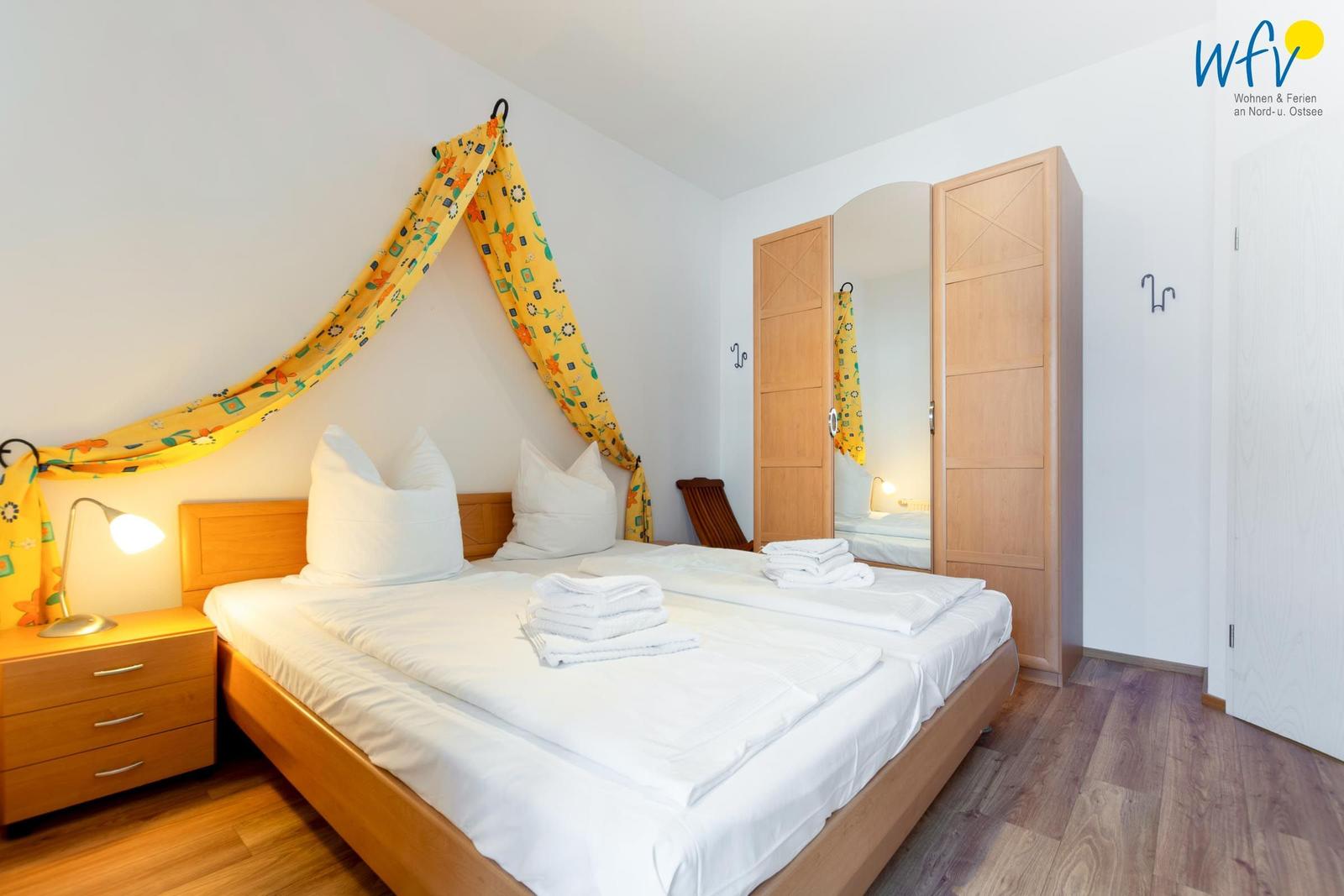 Schlafzimmer mit Doppelbett, Holzmöbel und gelbem Baldachin.
