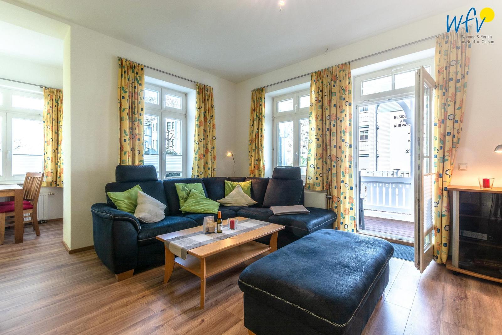 Wohnzimmer mit Sofa, Couchtisch und Balkontür. Gelbe Vorhänge und Holzboden.