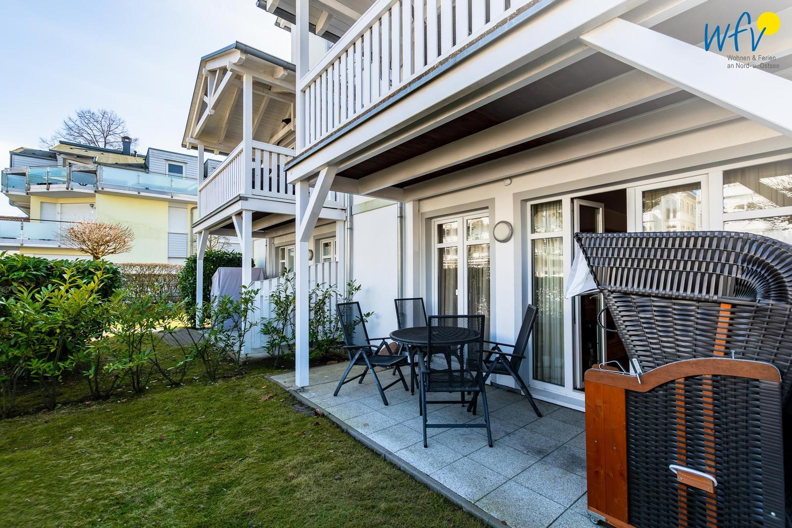Terrasse mit Tisch, Stühlen und Liegestuhl neben Haus mit Balkon.