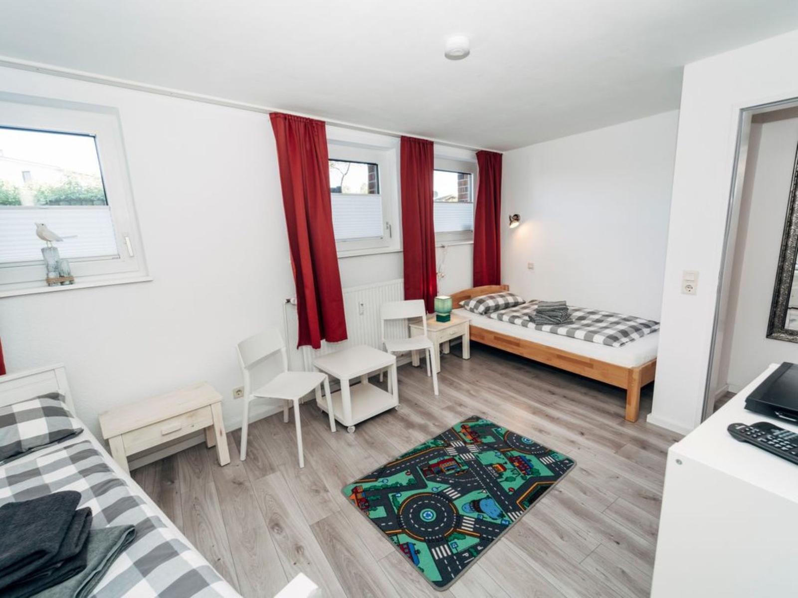 Zimmer mit zwei Betten, roten Vorhängen und Spielteppich auf Holzboden.