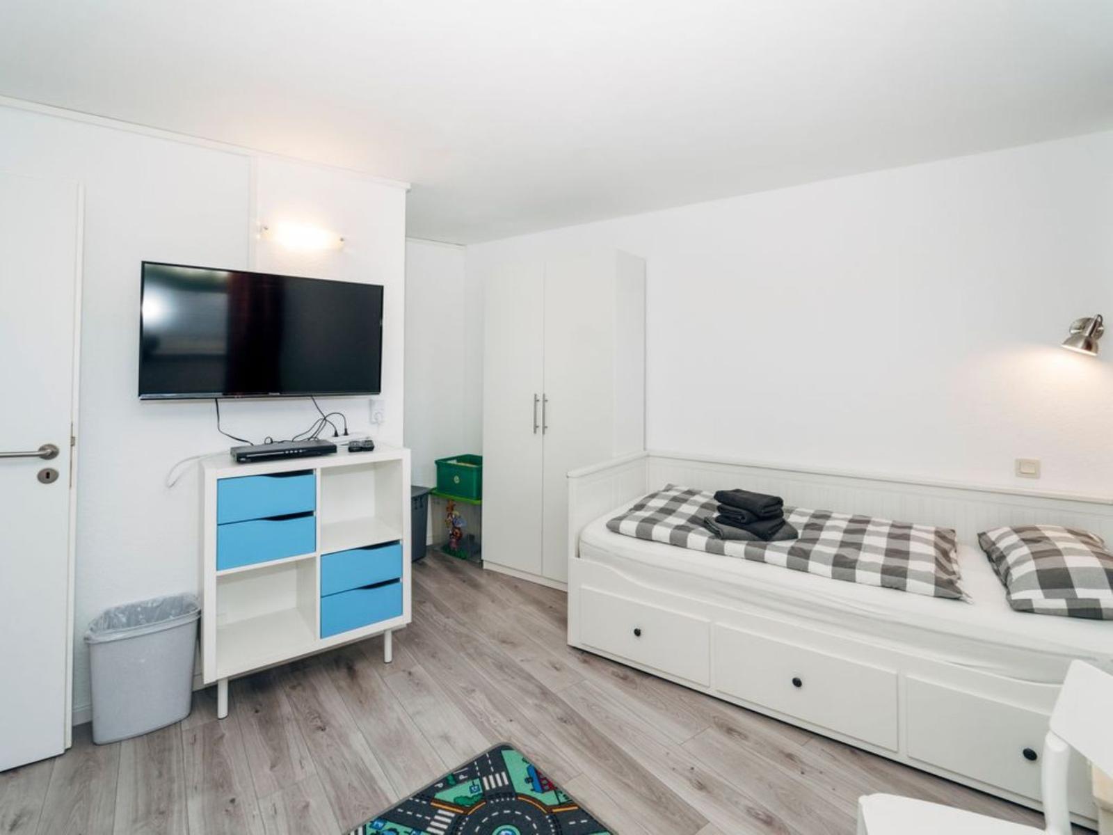 Ein Schlafzimmer mit Bett, Fernseher und Schrank. Holzboden und weiße Wände.