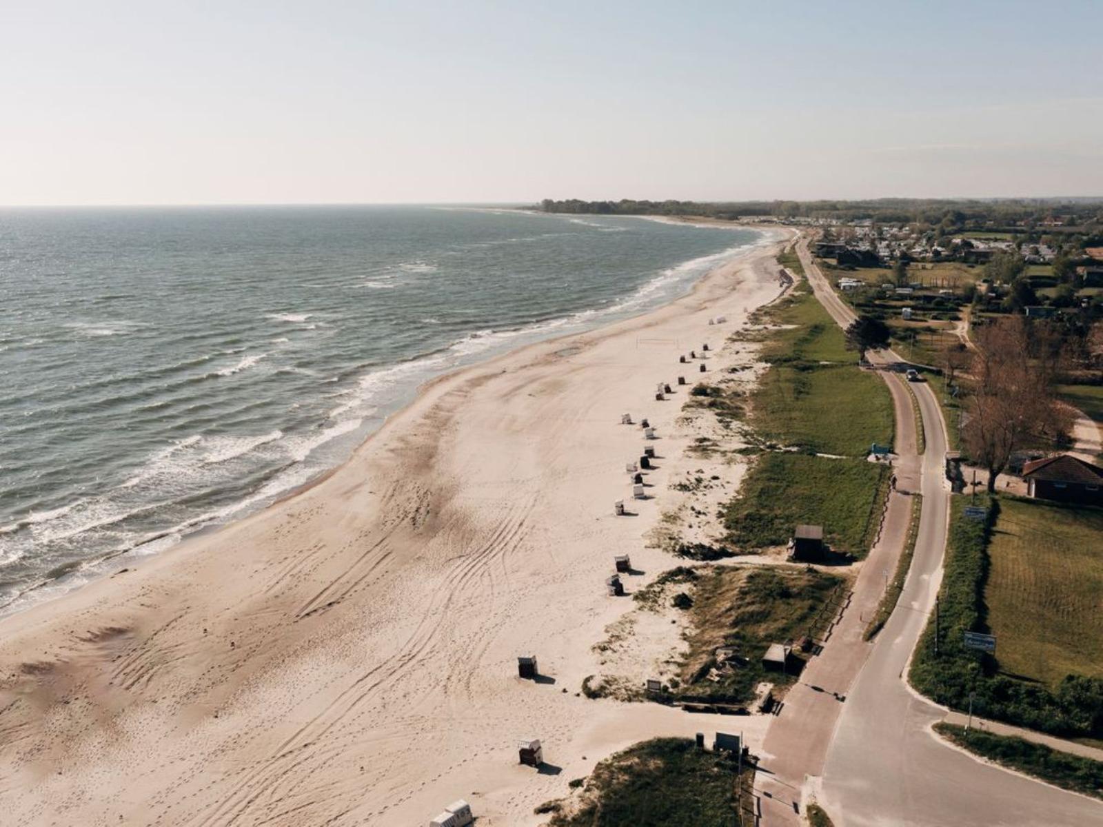 Strand mit Sand, Wellen und Strandkörben entlang einer Straße.