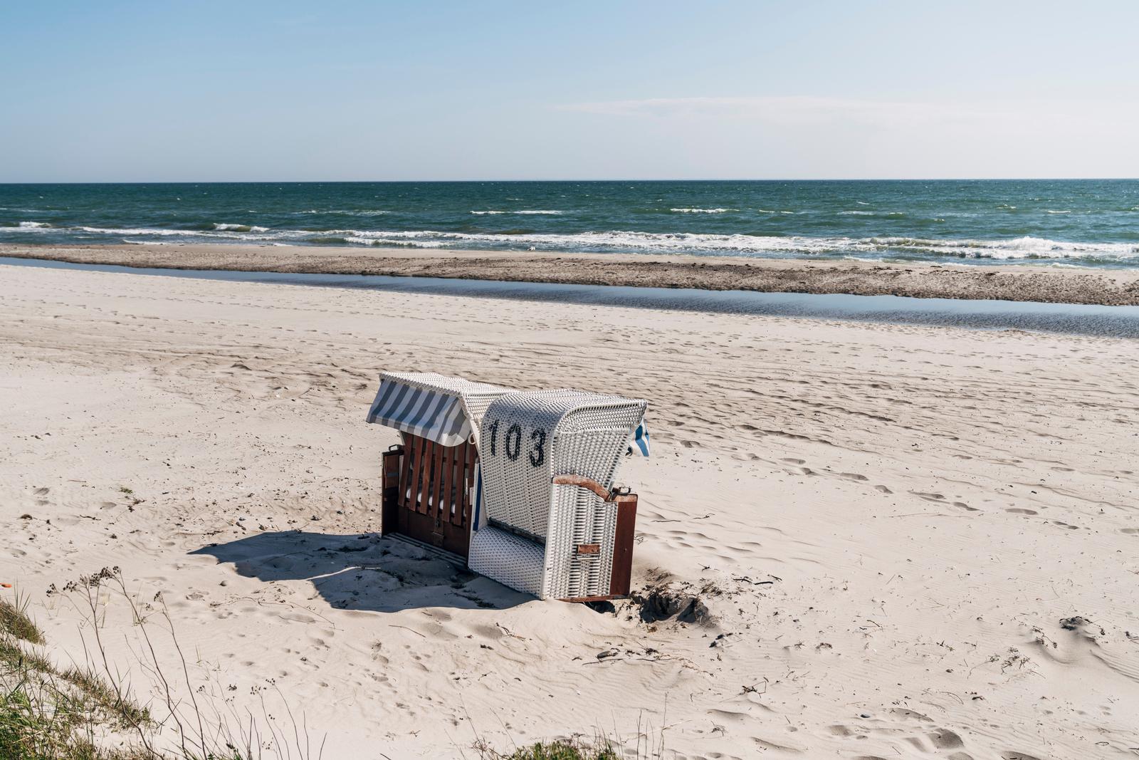 Strandkörbe mit Nummer 103 stehen auf dem Sand. Im Hintergrund das Meer.