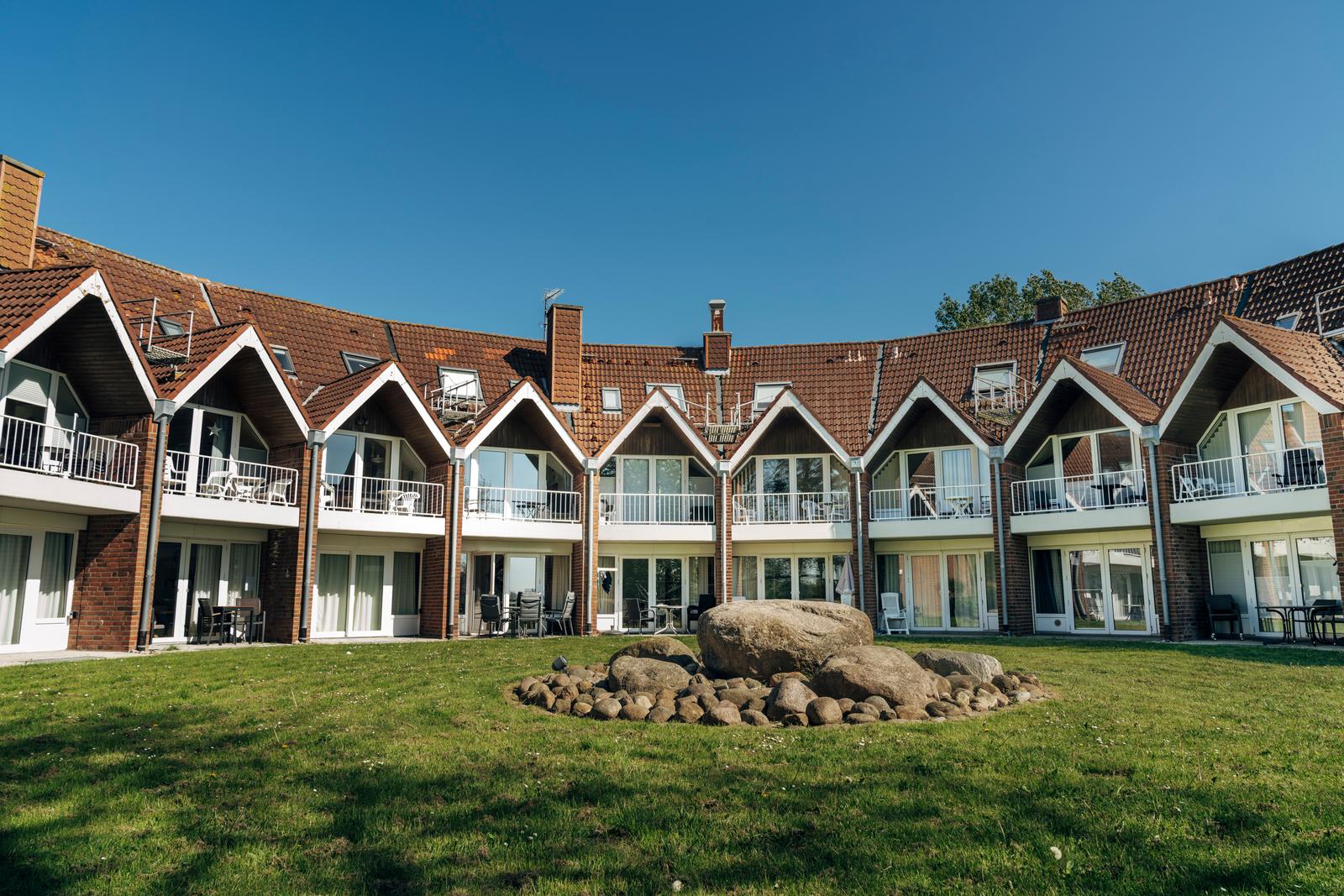 Ferienhaus mit Balkonen und grünem Garten. Zentraler Stein im Vordergrund.