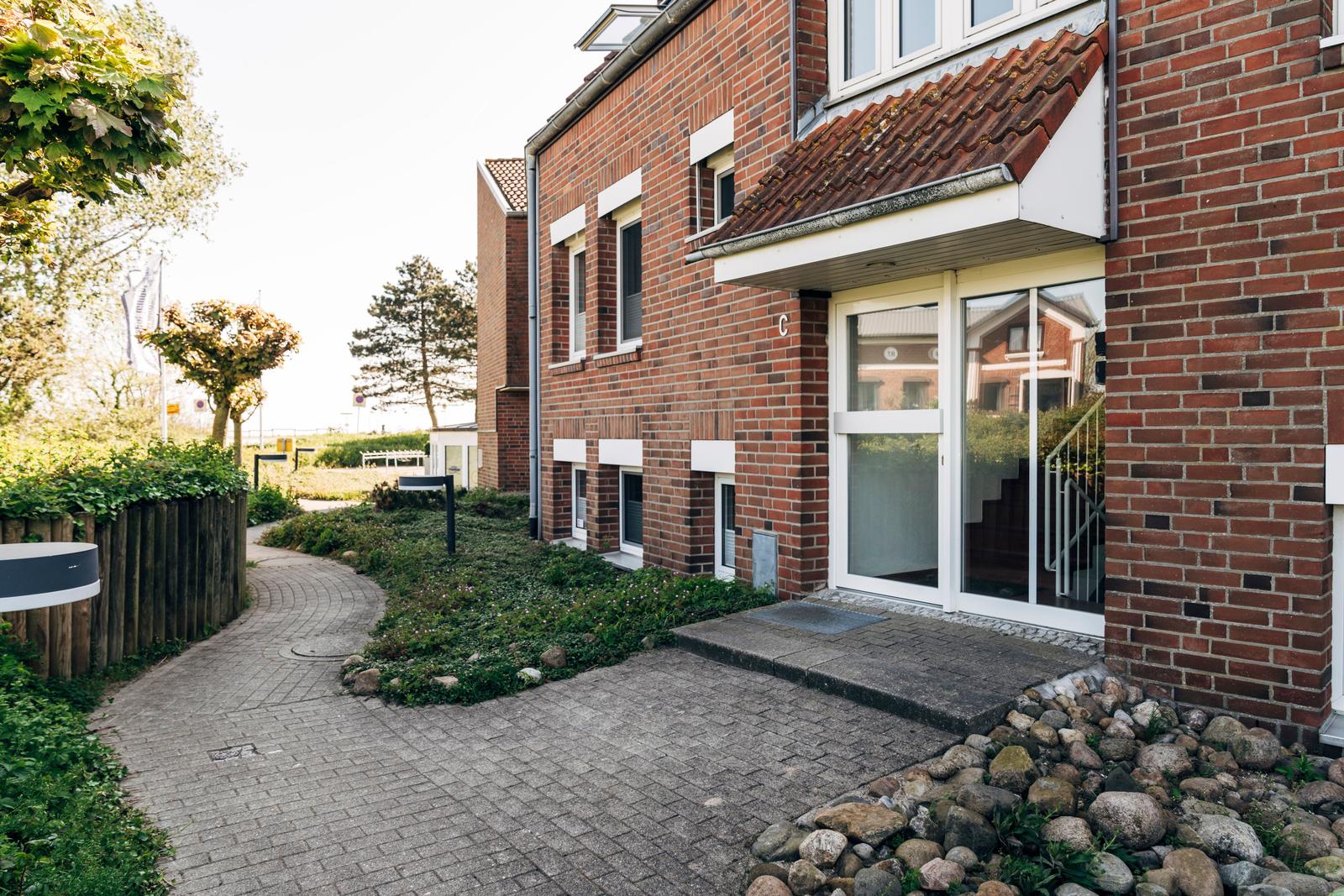 Haus mit rotem Ziegelstein, Glasfront und gepflastertem Weg durch Grünanlagen.