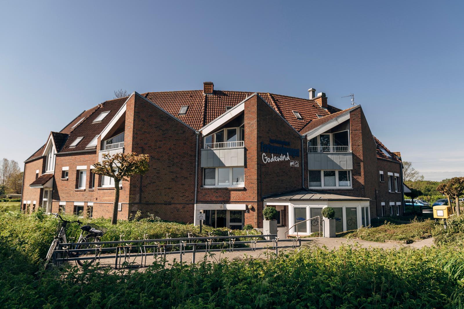 Ferienhaus Godewind mit rotem Ziegeldach und Balkonen. Grünanlage und Fahrräder vor dem Eingang.