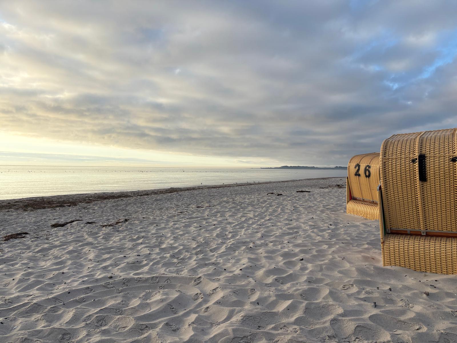 Strand mit Sandwellen und Strandkörben. Blick auf ruhiges Meer unter bewölktem Himmel.