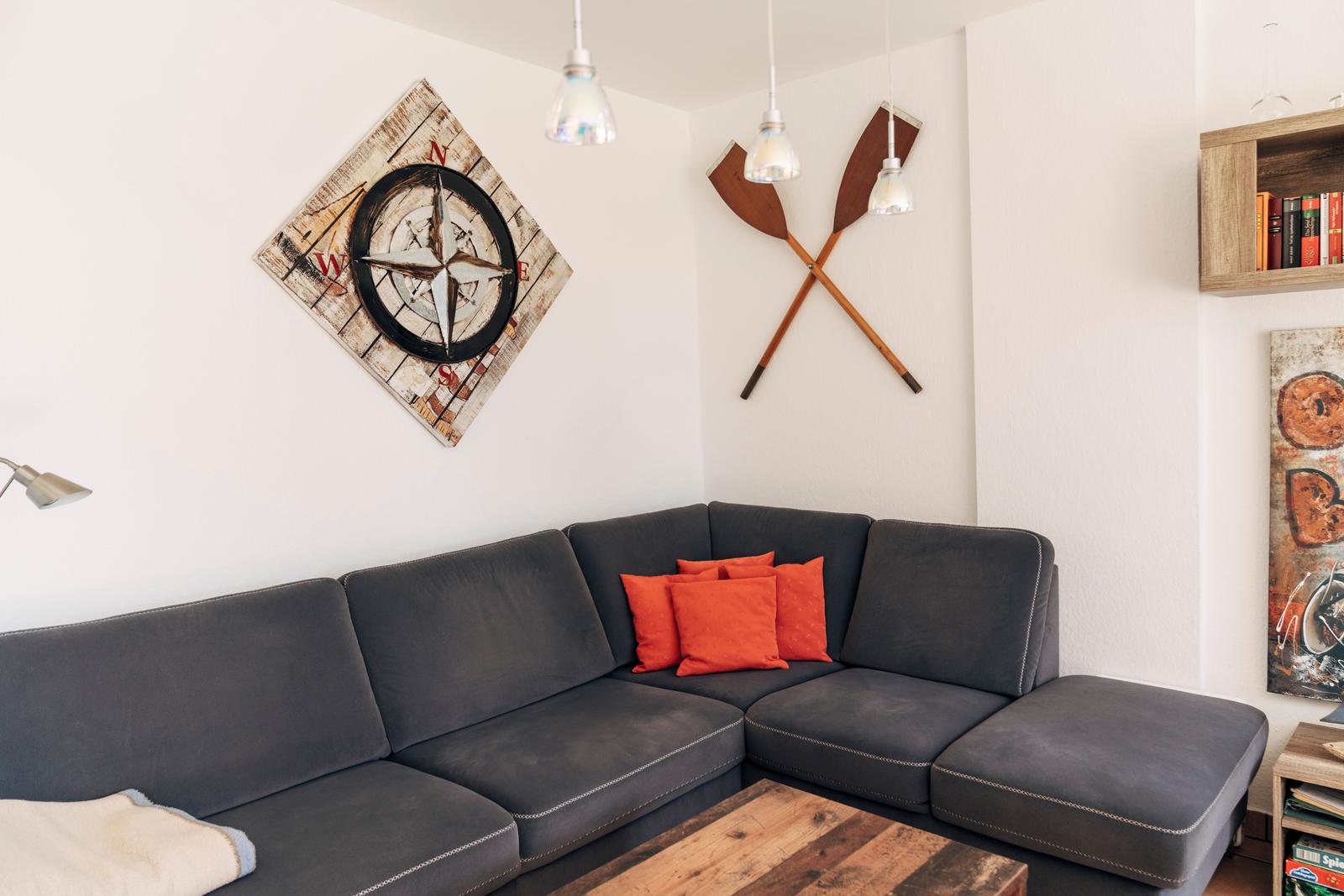 Ein Wohnzimmer mit grauem Sofa, orangefarbenen Kissen und einem Holztisch.