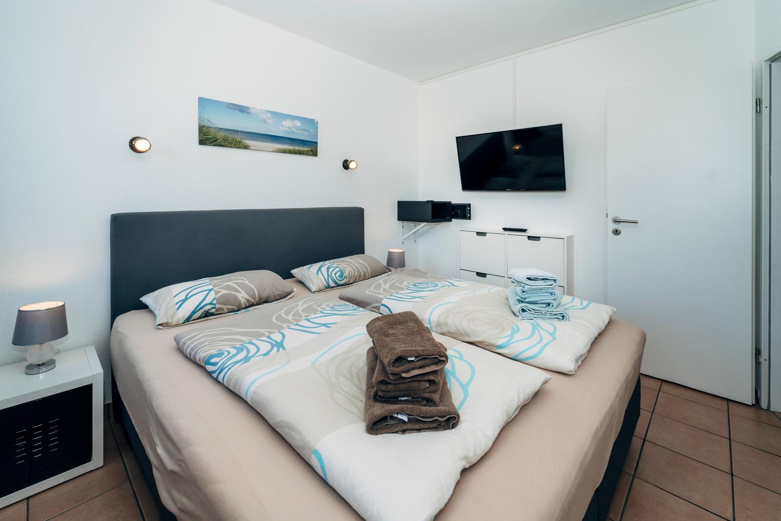 Schlafzimmer mit Doppelbett, Fernseher und Badetücher.