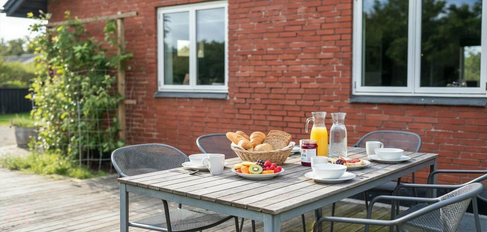 Außenbereich mit Tisch, Stühlen und Frühstück auf Holzterrasse vor Backsteinhaus