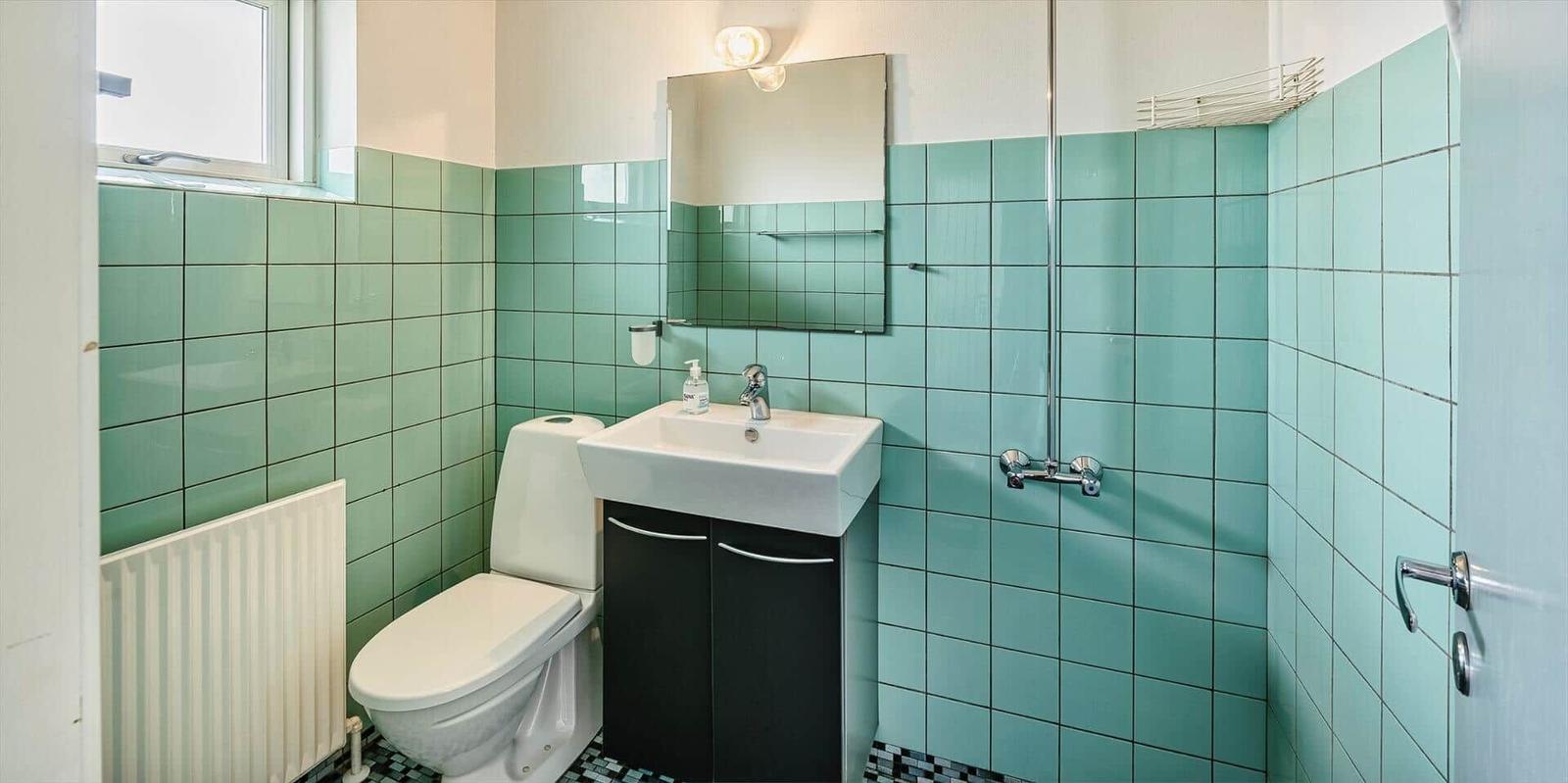 Badezimmer mit grünen Fliesen, Toilette, Waschbecken und Dusche.