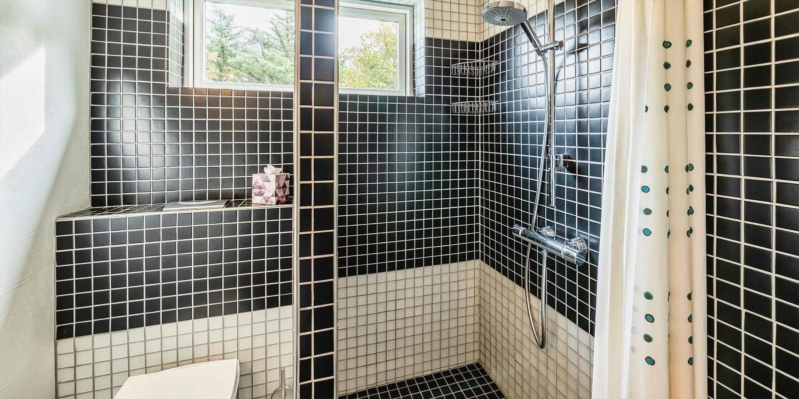 Dusche mit schwarzen und weißen Fliesen, Duschbrause und Fenster.