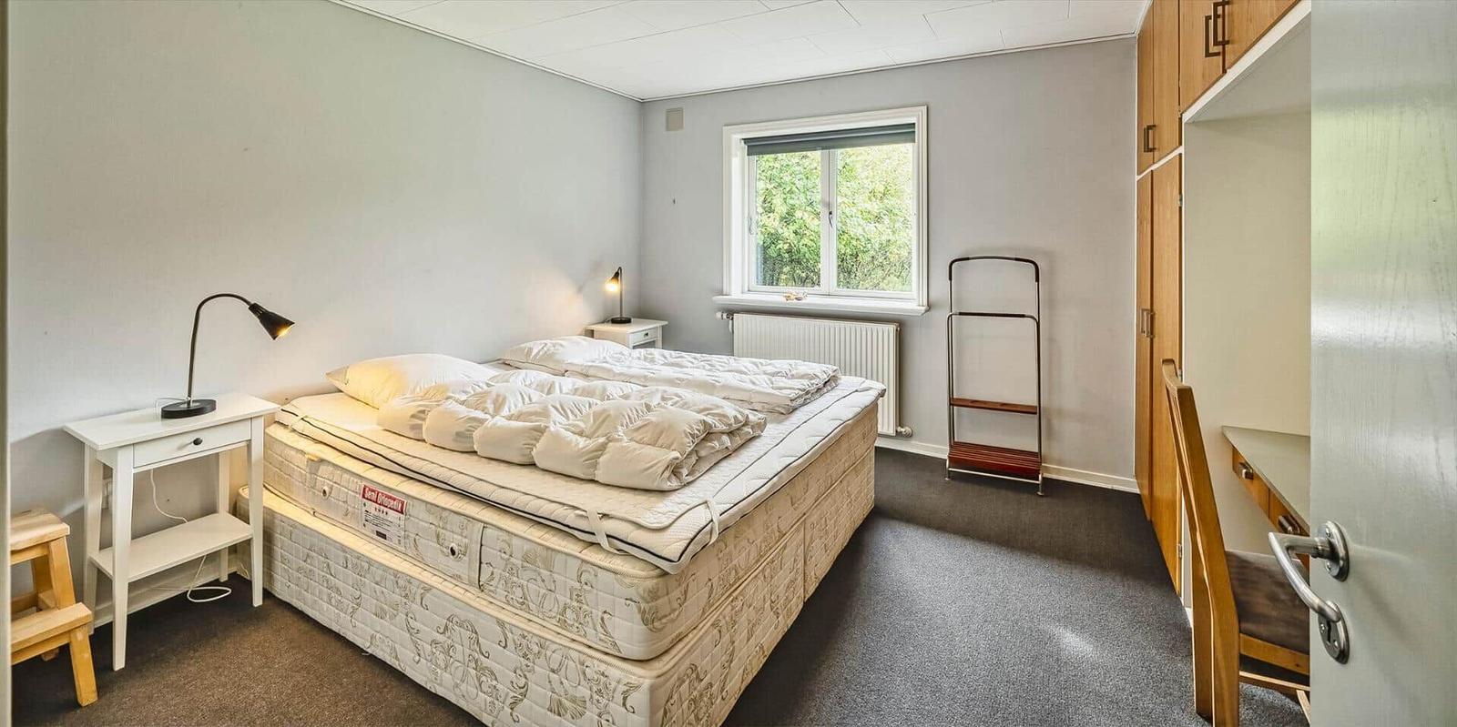 Schlafzimmer mit Bett, Nachttisch, Fenster und Kleiderschrank.