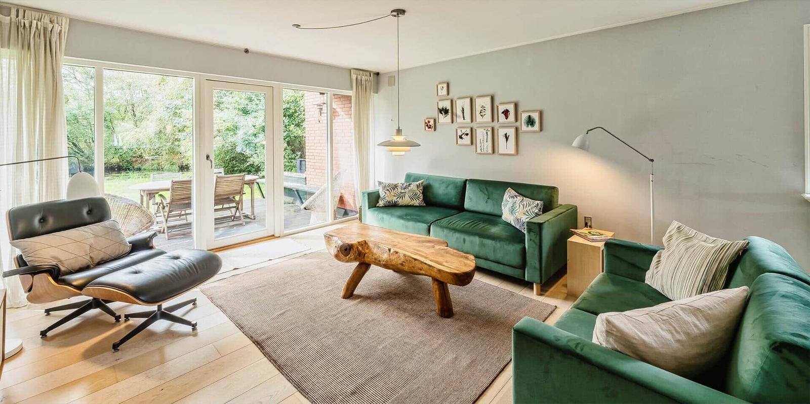Ein Wohnzimmer mit grünen Sofas, einem Holztisch und einer Terrasse mit Blick auf den Garten.
