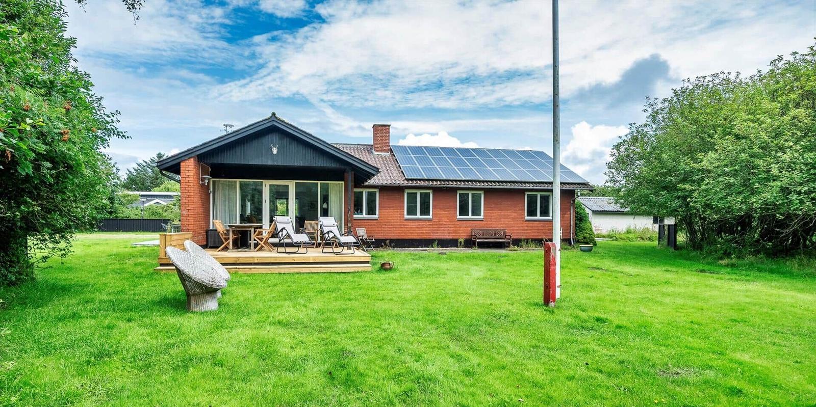 Rotes Haus mit Terrasse und Garten. Solaranlage auf Dach. Möbel im Freien.