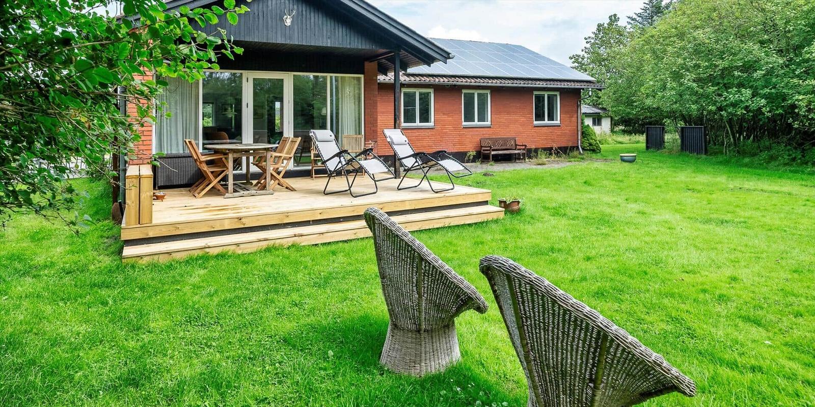 Haus mit Terrasse, Garten und Liegestühlen. Solaranlage auf Dach.