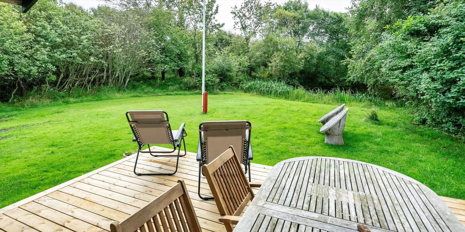 Terrasse mit Tisch und Stühlen, Blick auf grünen Rasen und Wald.