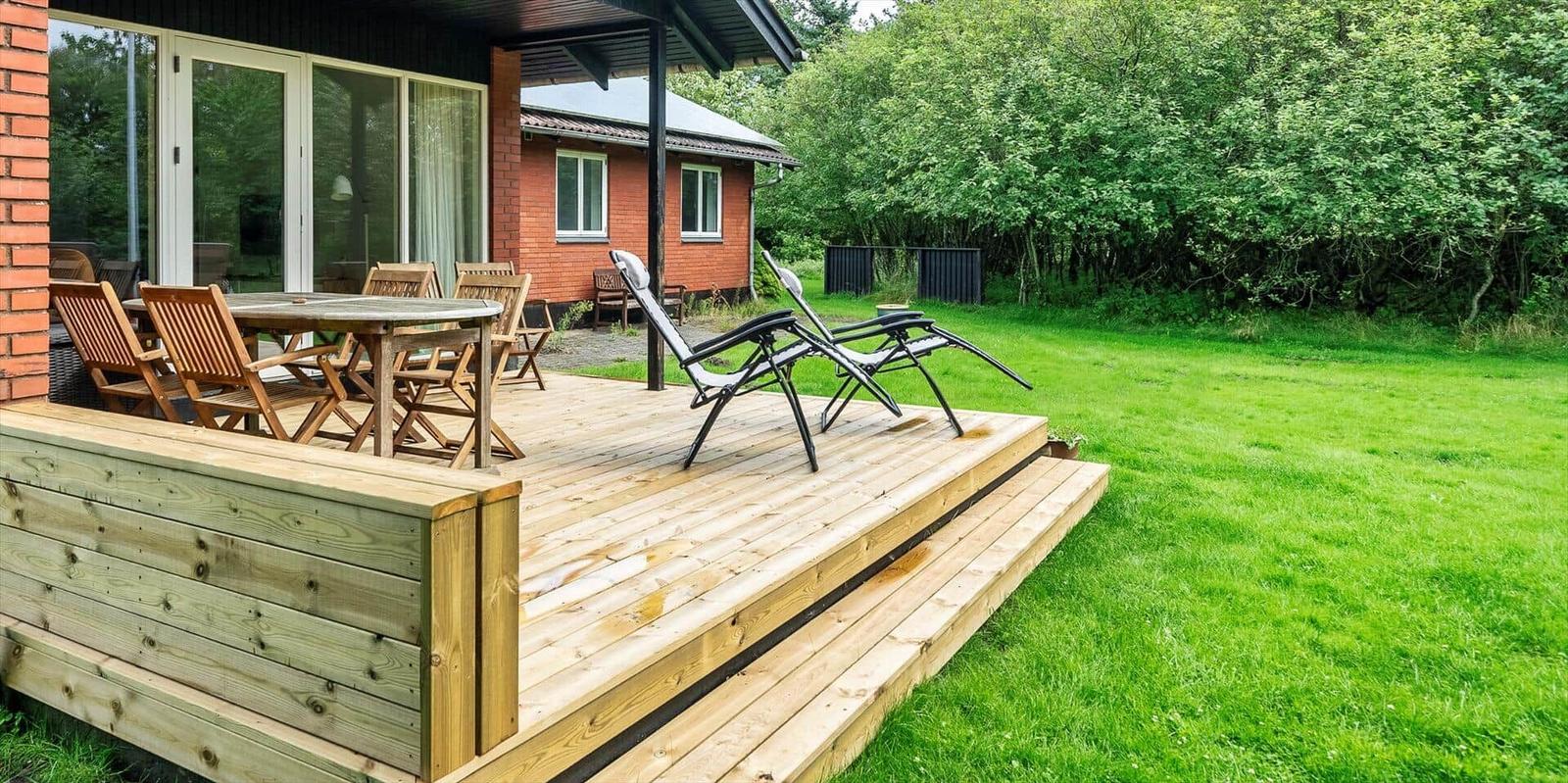 Terrasse mit Tisch, Stühlen und Liegestühlen neben einem Haus mit Garten.