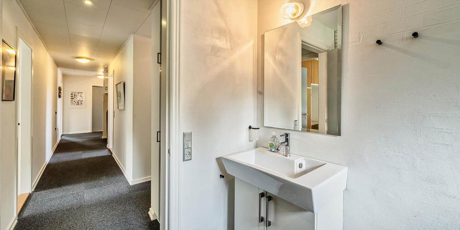Flur mit Waschbecken und Spiegel. Blick in den Flur mit Teppichboden.